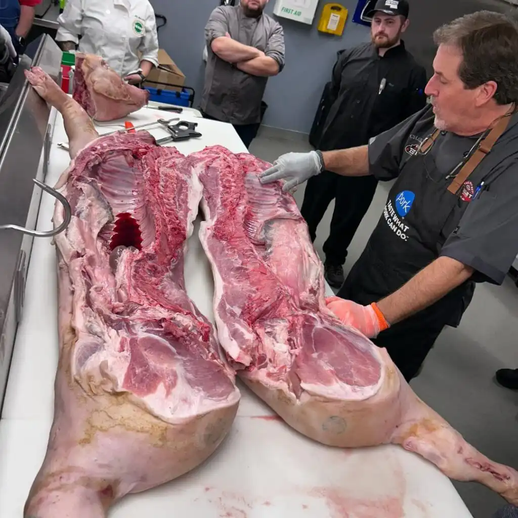 Chefs breaking down a whole pig on a stainless steel table